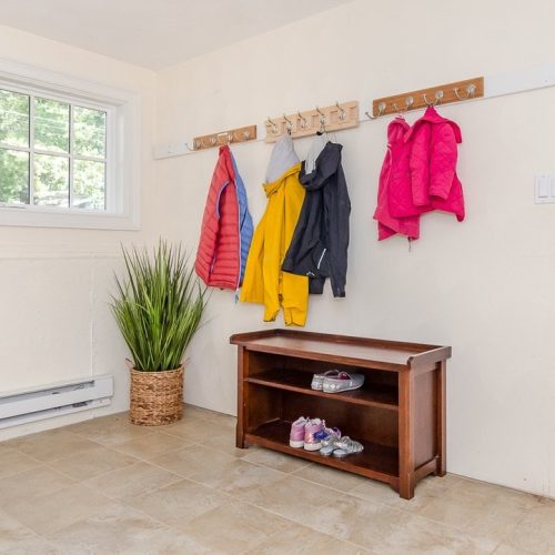 A neat mud room has childrens coat hung on wall pegs - an organized life, ma