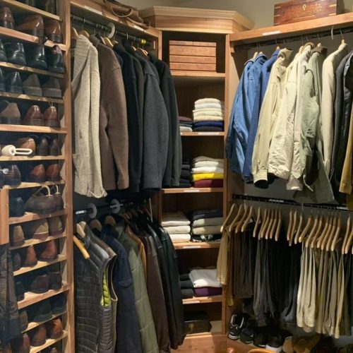 A man's walk-in closet is beautifully organized.