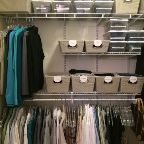 A closet has neatly hung clothes and labeled bins for storage.